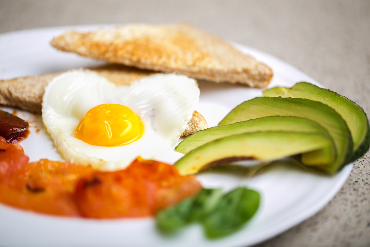 Healthy breakfast consisting of toast, eggs, avocado, fried tomato, and relish