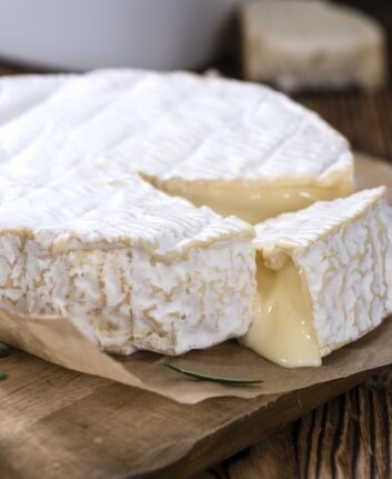 Portion of creamy Camembert (detailed close-up shot) on rustic wooden background