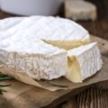 Portion of creamy Camembert (detailed close-up shot) on rustic wooden background