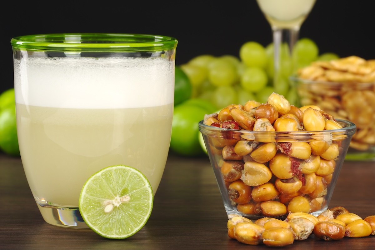 The Peruvian cocktail, Pisco Sour with the Peruvian snack, roasted corn, called cancha and grapes, limes, Pisco Sour and habas (roasted beans) in the background (Selective Focus, Focus on the front)
