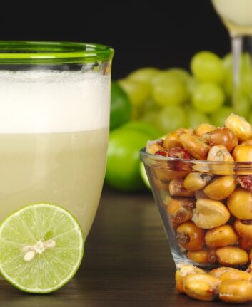 The Peruvian cocktail, Pisco Sour with the Peruvian snack, roasted corn, called cancha and grapes, limes, Pisco Sour and habas (roasted beans) in the background (Selective Focus, Focus on the front)