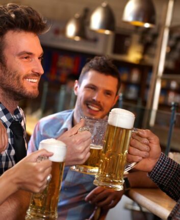 Happy young friends drinking beer, having fun in pub, smiling.