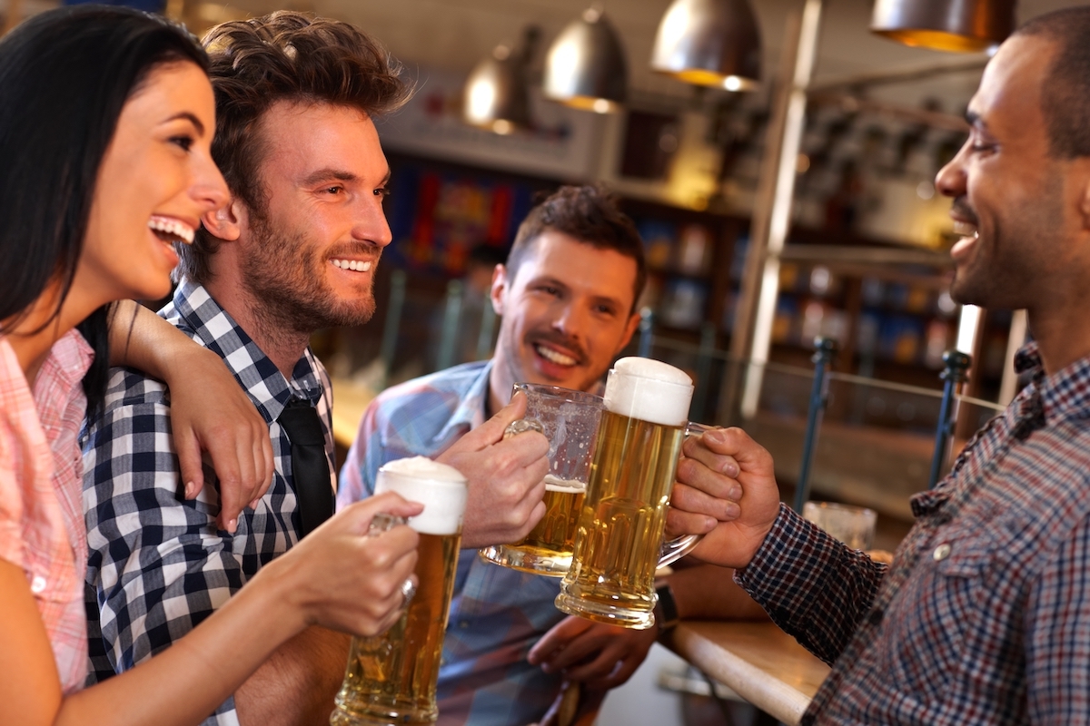 Happy young friends drinking beer, having fun in pub, smiling.