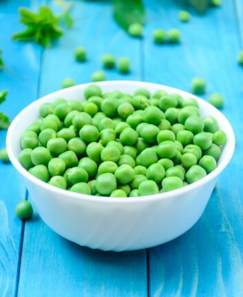 RAW baby peas in small white bowl, over colorful turquoise blue painted wooden boards. Close-up