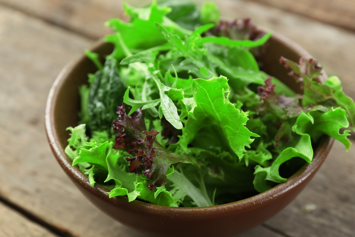 Bowl of mixed green salad on wooden table, closeup