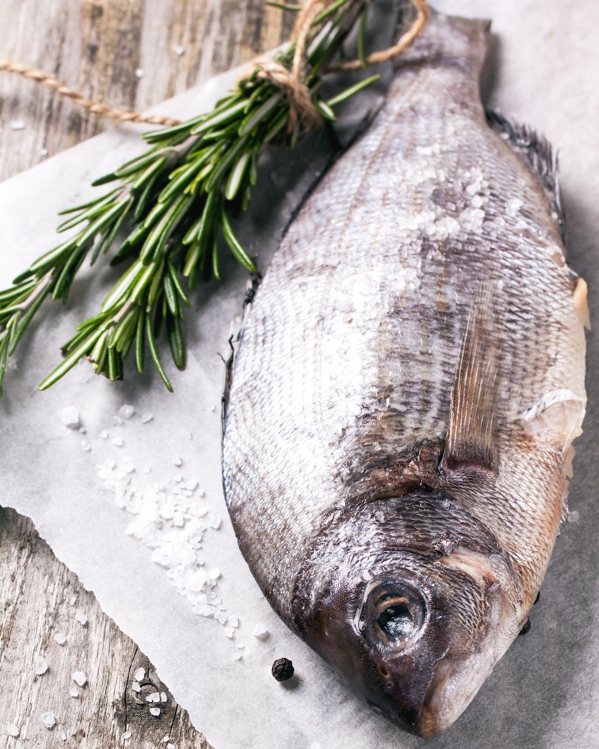 Raw dorado fish with rosemary and sea salt server on white paper over old wooden table. See series
