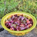 Colorful beet and citrus salad with pomegranate seeds in a green ceramic bowl outdoors on a stone surface.