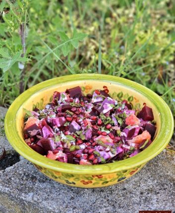 Colorful beet and citrus salad with pomegranate seeds in a green ceramic bowl outdoors on a stone surface.