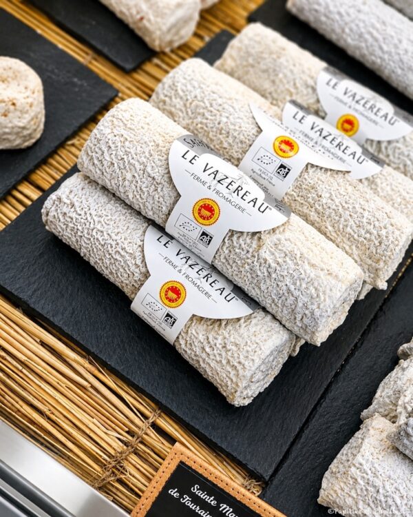 Rolled cylindrical cheeses with white rind labeled Le Vazereau, arranged on a black slate board.