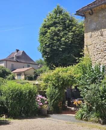 Entrée fleurie du restaurant Les Marronniers à Lanquais, avec maisons en pierre et ciel bleu