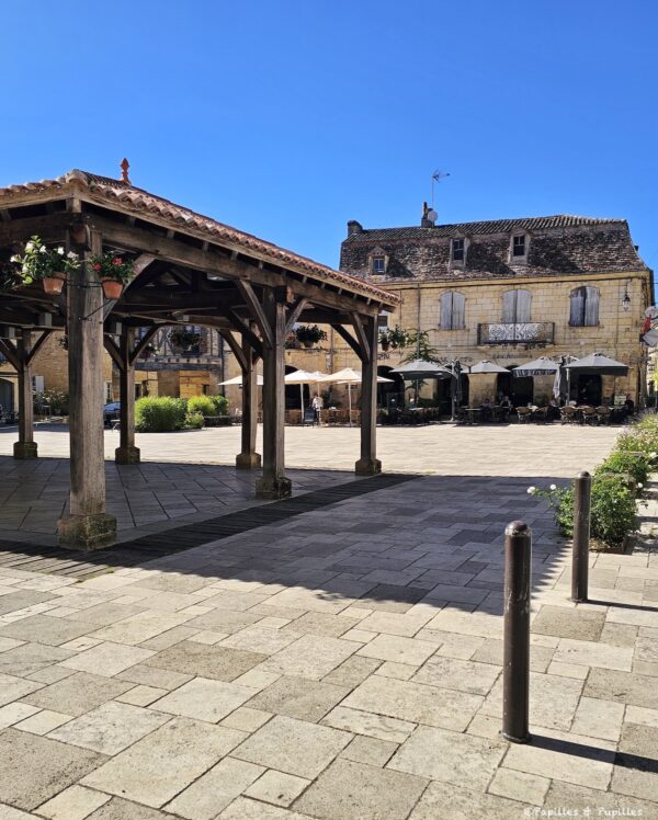 Place centrale de Beaumont-du-Périgord avec halle en bois, maisons anciennes et terrasses