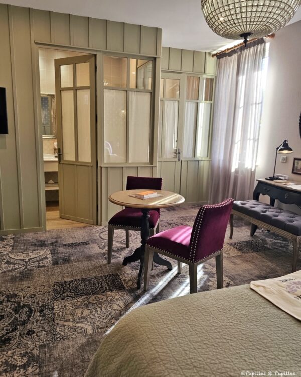 Chambre de l’hôtel Les Glycines avec verrière intérieure, fauteuils prune et lumière douce