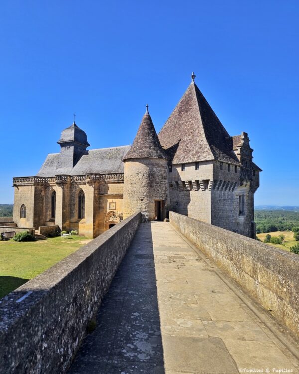 Chemin de ronde menant vers la chapelle du Château de Biron sous un grand ciel bleu