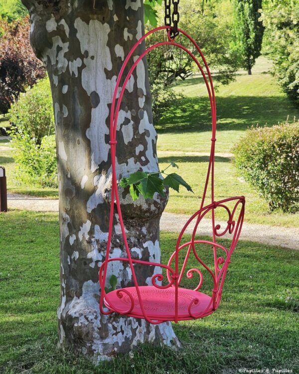 Fauteuil suspendu rose dans le jardin arboré de l’hôtel Les Glycines