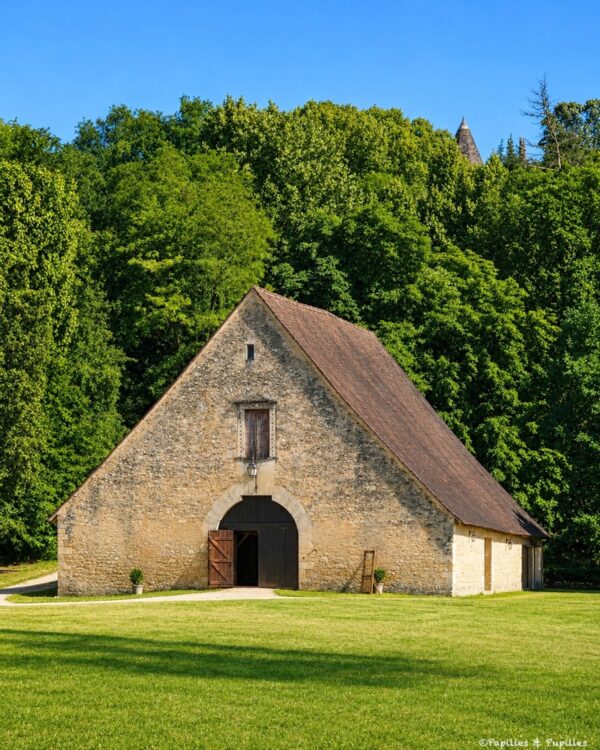 Grange aux dîmes de Lanquais en pierre blonde, entourée de pelouse et d’arbres sous un ciel bleu