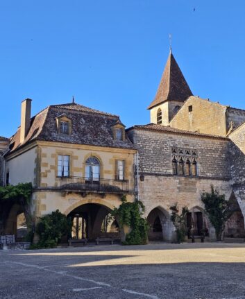 Place des Cornières à Monpazier avec arcades en pierre et clocher de l’église
