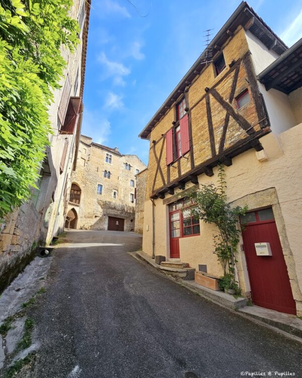 Maison à pans de bois et volets rouges dans une rue de Puy-l’Évêque