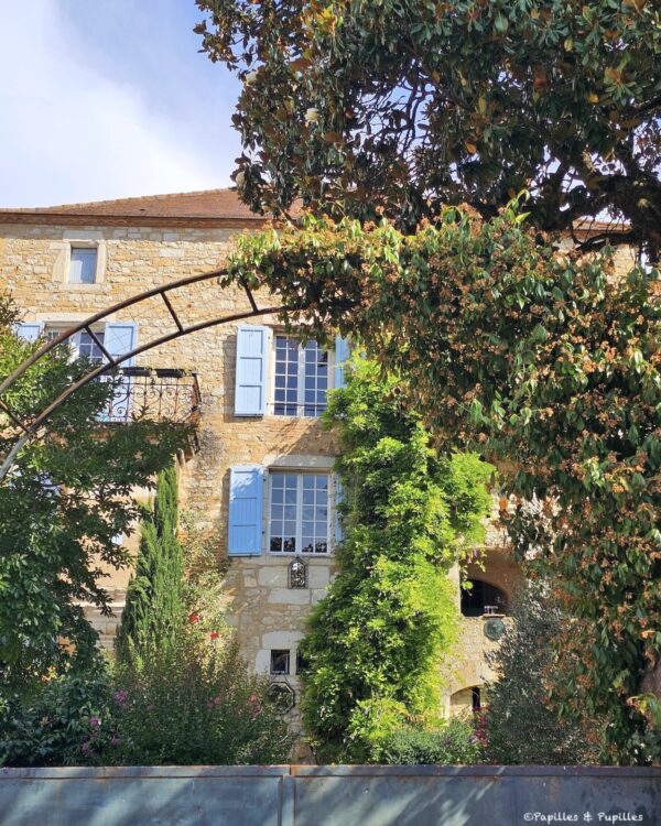 Façade en pierre avec volets bleus et jardin dans le centre de Puy-l’Évêque