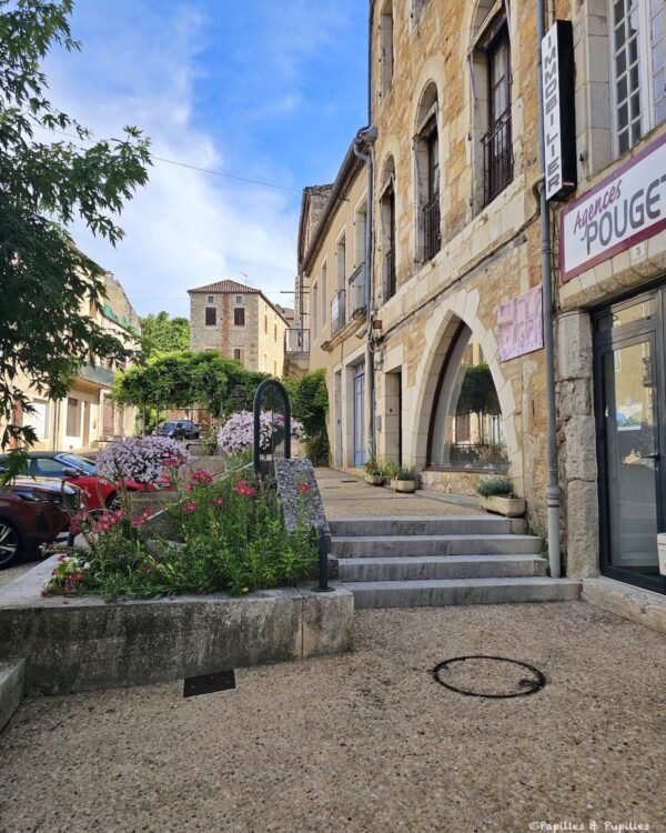 Rue de Puy-l’Évêque avec commerces, façades en pierre et fleurs