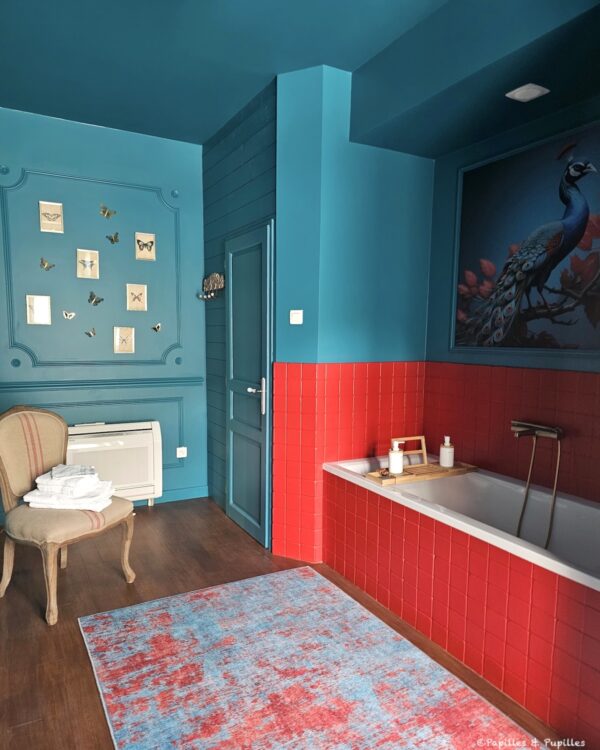 Salle de bains bleu canard et rouge du Domaine de Sens Bas avec baignoire et décor de paon