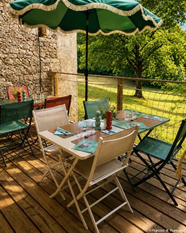 Terrasse ombragée du Domaine de Sens Bas avec tables dressées et vue sur la prairie