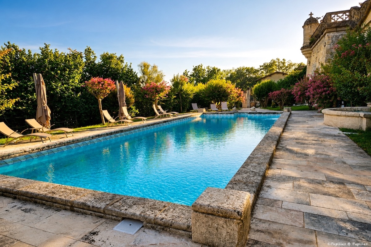 Piscine du Château de La Rivière à Fronsac, bordée de transats et de fleurs